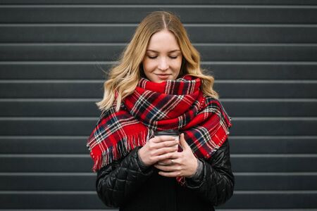 Happy woman with a scarf. Autumn. Portrait of the beautiful girl. Office building. Fashionable portrait of a girl model with waving red scarf. Autumn portrait in the cityの写真素材