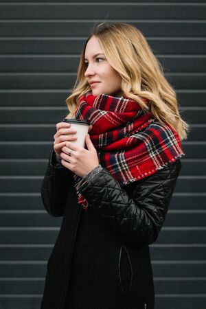 Happy woman with a scarf. Autumn. Portrait of the beautiful girl. Office building. Fashionable portrait of a girl model with waving red scarf. Autumn portrait in the cityの写真素材