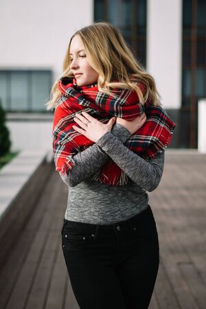 Happy woman with a scarf. Autumn. Portrait of the beautiful girl. Office building. Fashionable portrait of a girl model with waving red scarf. Autumn portrait in the cityの写真素材