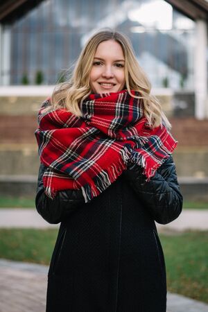 Happy woman with a scarf. Autumn. Portrait of the beautiful girl. Office building. Fashionable portrait of a girl model with waving red scarf. Autumn portrait in the cityの写真素材