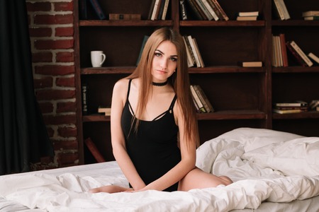 Portrait of beautiful smiling exotic young woman lying in bed in her underwear with chokerの写真素材