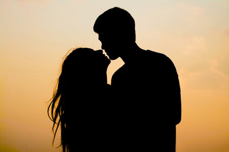 Silhouette young couple kissing over sunset background.の写真素材