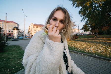 Young fashion funny woman eating hamburger outdoor on the street.の写真素材