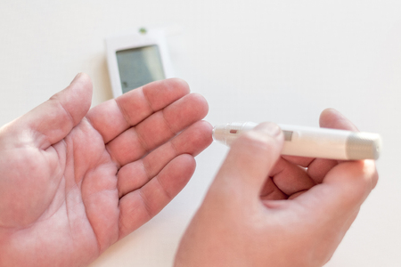 Medicine, diabetes, glycemia, health care and people concept - Close up of man hands using lancet on finger to check high blood sugar level with glucometer or glucose meter at home.の写真素材