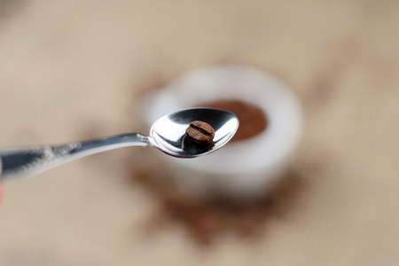 Spoon with coffee beans and cup full of coffee beans on the cloth sack background.の写真素材