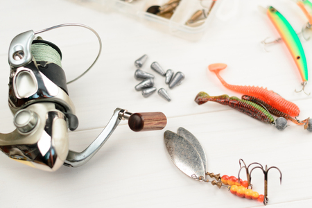 Fishing rod with reel, spoon baits, tackles and wobblers in box for catching or fishing a predatory fish on white vintage wooden background.の写真素材