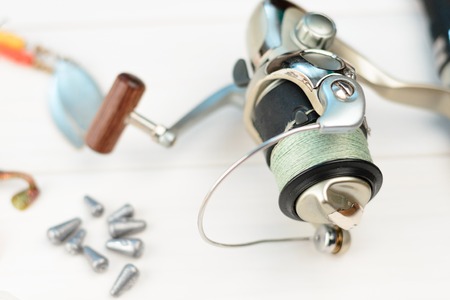 Fishing rod with reel, spoon baits, tackles and wobblers in box for catching or fishing a predatory fish on white vintage wooden background.の写真素材
