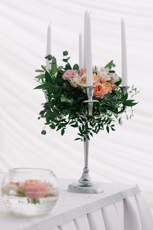 Beautiful wedding floral decoration on a table in a restaurant. White tablecloths, bright room, candles, close-up shooting. The event, happiness, honeymooners. Soft bokeh white background.の写真素材
