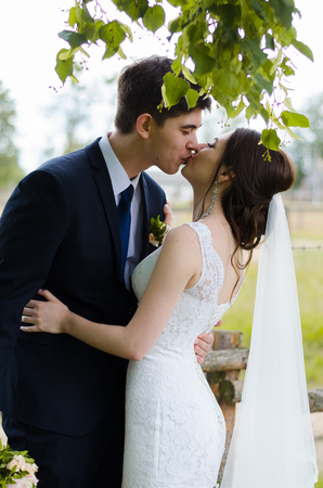 A beautiful married couple in wedding dresses, posing for a photo shooting in an belarusian village near the fence, with a wedding bouquet.の写真素材