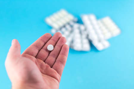 The man hand is holding a pill with copy space on blue background. Focus on foreground, soft bokeh.の写真素材