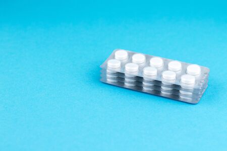 Packs of white pills packed in blisters with copy space on blue background. Focus on foreground,...