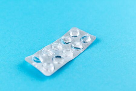 Empty pack of white pills packed in blister with copy space on blue background. Focus on foreground, soft bokeh.の写真素材