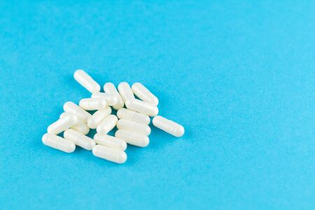 Close up white capsules on blue background with copy space. Focus on foreground, soft bokeh....