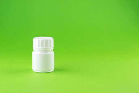Close up white pill bottle on green background with copy space. Focus on foreground, soft bokeh. Pharmacy drugstore concept.の写真素材