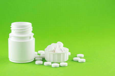 Close up white pill bottle with spilled out pills and capsules in cap on green background with copy space. Focus on foreground, soft bokeh. Pharmacy drugstore concept.の写真素材