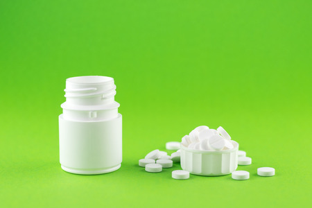 Close up white pill bottle with spilled out pills and capsules in cap on green background with copy space. Focus on foreground, soft bokeh. Pharmacy drugstore concept.の写真素材