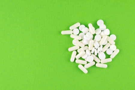 Close up white pills and capsules on green background with copy space. Focus on foreground, soft...