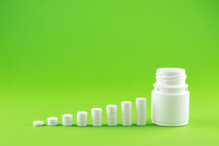 Close up pyramid concept of white pills and bottle on green background with copy space. Focus on foreground, soft bokeh. Pharmacy drugstore concept.の写真素材