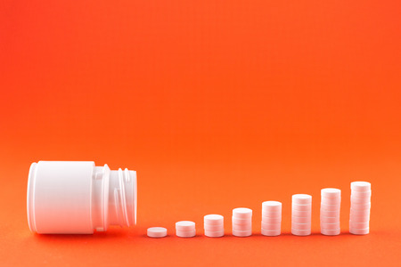 Close up pyramid concept of white pills and bottle on orange background with copy space. Focus on foreground, soft bokeh. Pharmacy drugstore concept.の写真素材