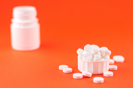Close up white pill bottle with spilled out pills and capsules in cap on orange background with copy space. Focus on foreground, soft bokeh. Pharmacy drugstore concept.の写真素材