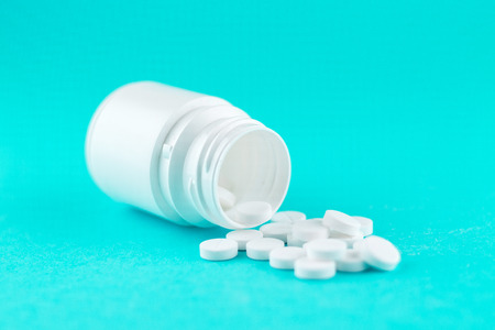 Close up white pill bottle with spilled out pills on turquoise background with copy space.の写真素材