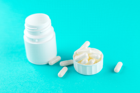 Close up white pill bottle with spilled out pills and capsules in cap on turquoise background with copy space.の写真素材