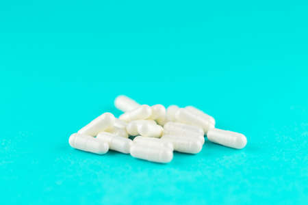 Close up white capsules on turquoise background with copy space.