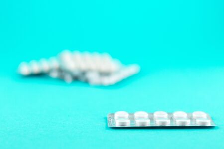 Packs of white capsules and pills packed in blisters with copy space on turquoise background.の写真素材