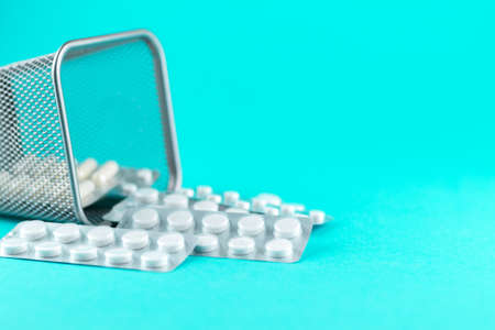 Trash bin with packs of white capsules and pills packed in blisters with copy space on turquoise background.の写真素材