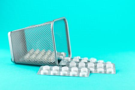 Trash bin with packs of white capsules and pills packed in blisters with copy space on turquoise background.の写真素材