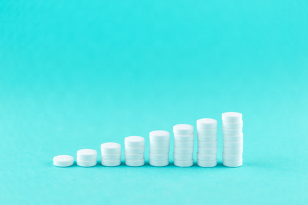 Close up pyramid concept of white pills on turquoise background with copy space. Focus on foreground, soft bokeh. Pharmacy drugstore concept.の写真素材