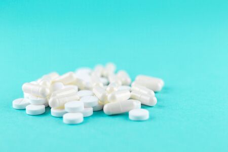Close up white pills and capsules on turquoise background with copy space. Focus on foreground, soft bokeh. Pharmacy drugstore concept.の写真素材