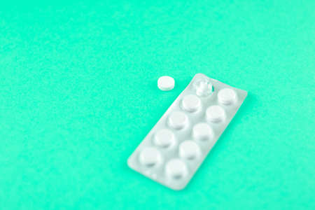 Packs of white pills packed in blisters with copy space on aquamarine background. Focus on foreground, soft bokeh.の写真素材