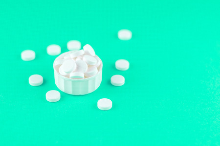 Close up white pills and capsules in cap on aquamarine background with copy space. Focus on...