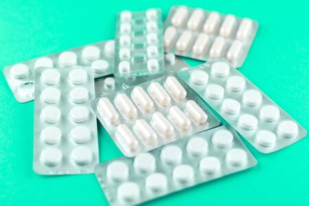 Packs of white capsules and pills packed in blisters with copy space on aquamarine background. Focus...
