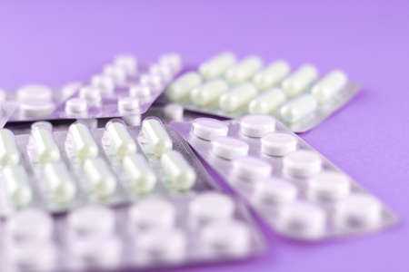 Packs of white capsules and pills packed in blisters with copy space on purple background. Focus on...