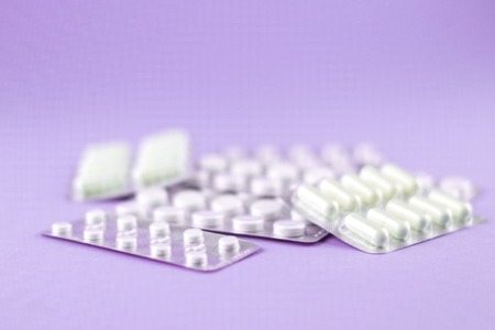 Packs of white capsules and pills packed in blisters with copy space on purple background. Focus on...