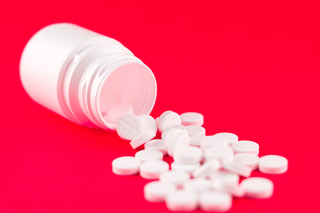 Close up white pill bottle with spilled out pills on candy apple background with copy space. Focus on foreground, soft bokeh. Pharmacy drugstore concept.の写真素材