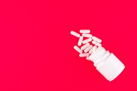Close up white pill bottle with spilled out pills and capsules in cap on candy apple background with copy space. Focus on foreground, soft bokeh. Pharmacy drugstore concept. Top view.の写真素材