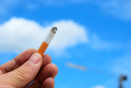 This is a cigarette in the smoker hand with blue skyの写真素材