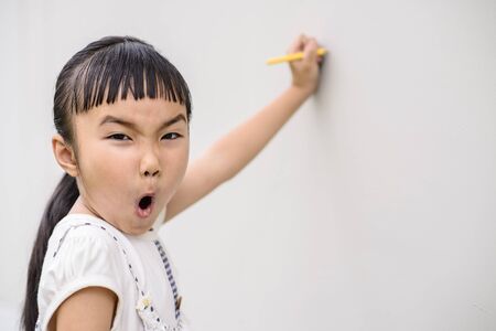 Kid with surprise pose and mood while writing on wallの写真素材