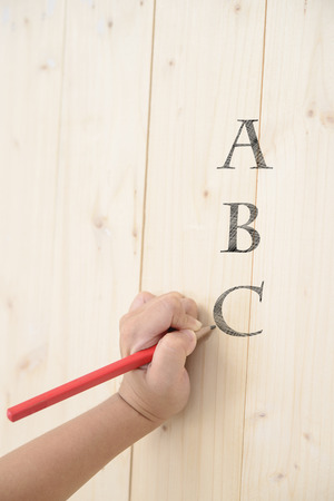 Kid hand hold red pencil and writing abc on wood wallの写真素材