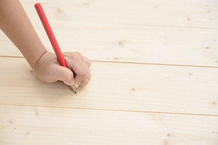 Kid hand hold red pencil and writing on wood floorの写真素材