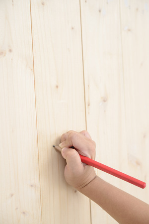 Kid hand hold red pencil and writing on wood floorの写真素材