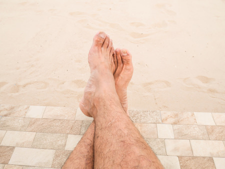 Man is relaxing barefoot at the beach. Closeup legs of Asia man's skin and men hairy legs on sand background. Guy's legs on the sand.のeditorial素材