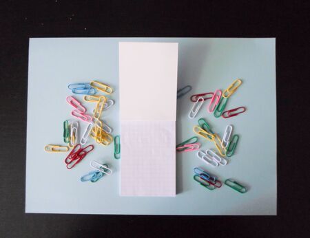 colored paper clips and paper for notes on a white sheet of paper on a black background. place to write.の写真素材
