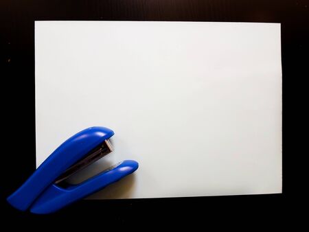 blue stapler and white paper on a black table. place to write. stationery.