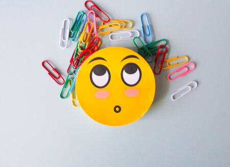 colored paper clips on a white sheet of paper and a yellow emoticon. view from aboveの写真素材