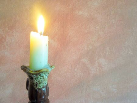 a burning candle stands in front of a pink wallの写真素材