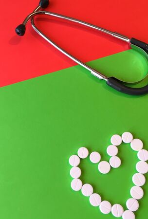 Top view of stethoscopes, pills in the shape of a heart on a green and red background, medical and healthy concept.の写真素材